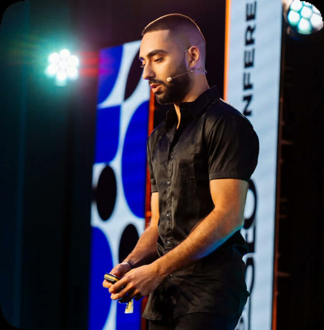 Kasra Dash speaking on a conference stage with a headset microphone